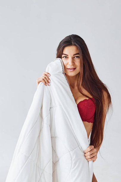 Woman in red underwear covering her body by towel in the studio against white background. - Фото, изображение