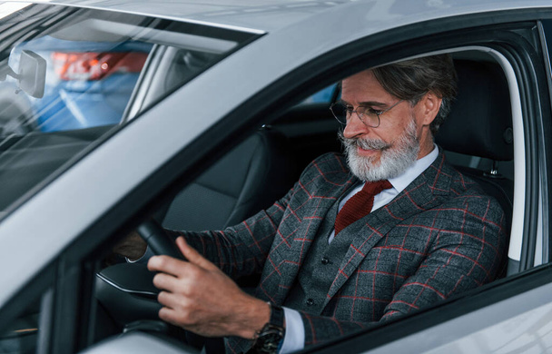 Moderni tyylikäs vanhempi mies harmaine hiuksineen ja viiksineen on modernissa autossa. - Valokuva, kuva