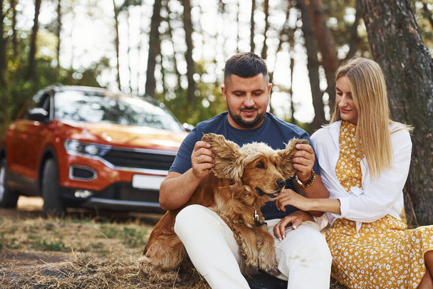 Couple with dog have weekend outdoors in the forest with car behind them. - 写真・画像