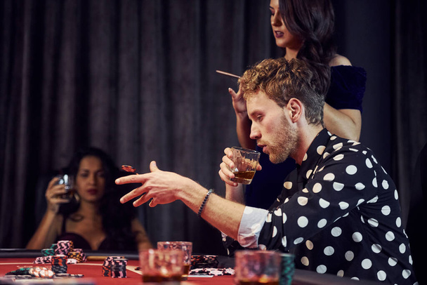 Con vasos de bebida. Grupo de jóvenes elegantes que juegan al póquer en el casino juntos. - Foto, Imagen