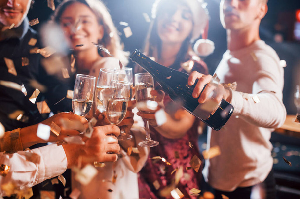 Group of cheerful friends celebrating new year indoors with drinks in hands. - Foto, Imagen