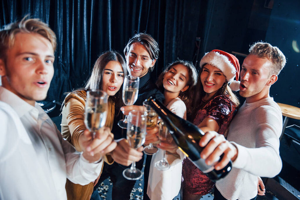 Takes selfie. Group of cheerful friends celebrating new year indoors with drinks in hands. - Foto, Bild