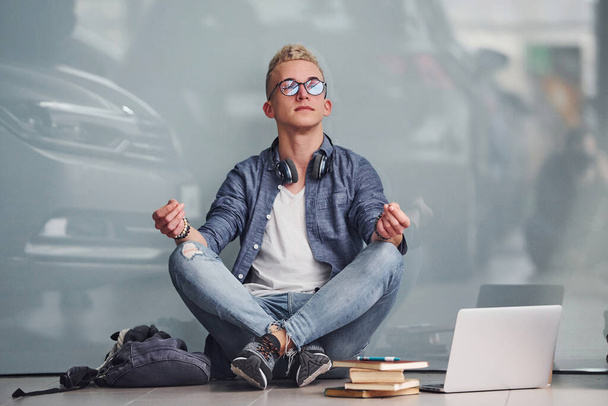 Young hipster guy sitting indoors near grey background with laptop and books. - Foto, Imagem