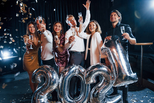 Confetti is in the air. Cheerful group of people with drinks and balloons in hands celebrating new 2021 year. - Fotoğraf, Görsel