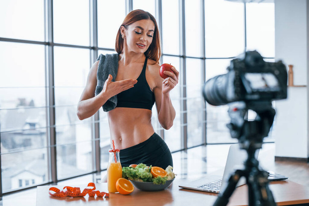 Female vlogger with sportive body standing indoors near table with healthy food. - Фото, зображення