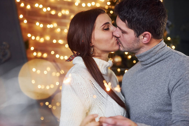 Couple kissing indoors in christmas decorated room with sparklers in hands. - Fotó, kép