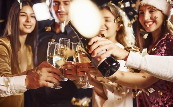 Pouring champagne. Group of cheerful friends celebrating new year indoors with drinks in hands. - Fotoğraf, Görsel