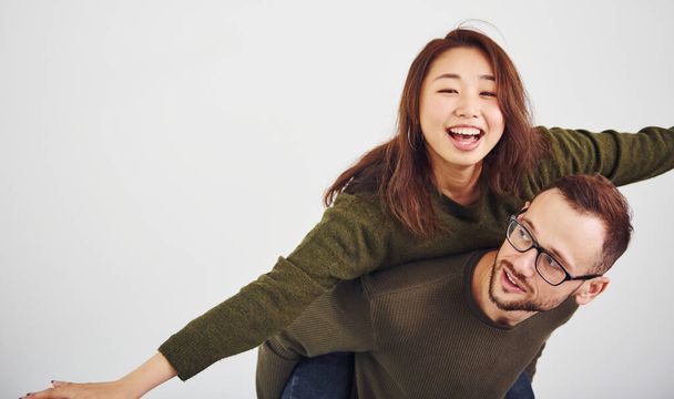 Happy multi ethnic couple in casual clothes have fun together indoors in the studio. Caucasian guy with asian girlfriend. - 写真・画像