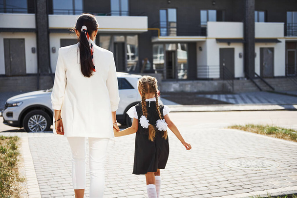 Mother with daughter in school uniform outdoors near white car. - Foto, imagen