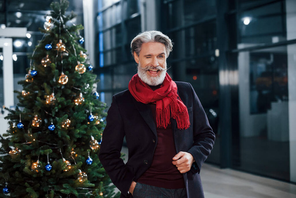 Portrait of fashionable old man with grey hair and mustache standing near christmas decorated tree. - Zdjęcie, obraz