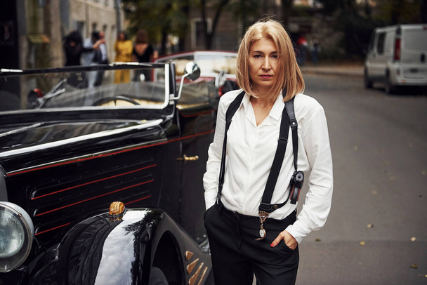 Blonde woman in black retro clothes near old vintage classic car. - Valokuva, kuva