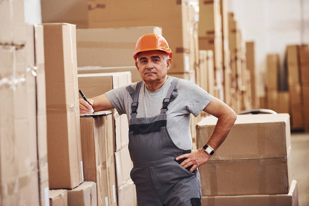 Senior storage worker in uniform and notepad in hands checks production. - 写真・画像