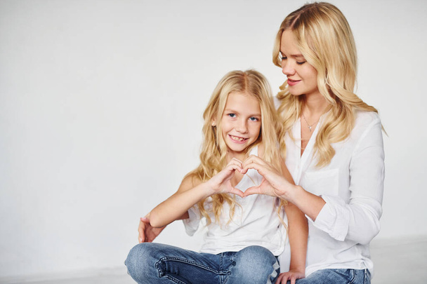 Mother with her daughter together shows love gesture in the studio with white background. - Photo, Image