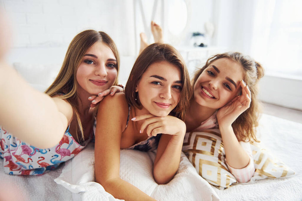 Making selfie. Happy female friends having good time at pajama party in the bedroom. - Fotó, kép