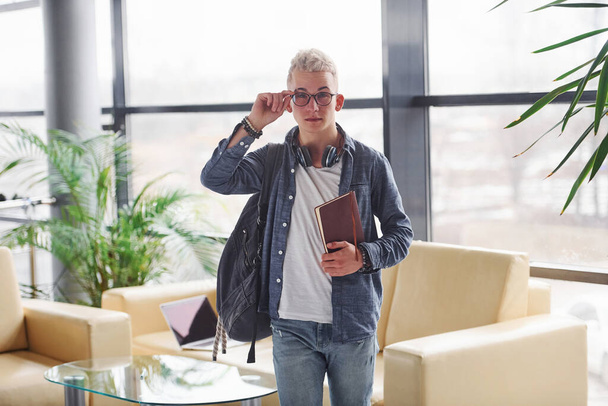 Young hipster guy in nice clothes standing indoors with notepad. - Foto, afbeelding