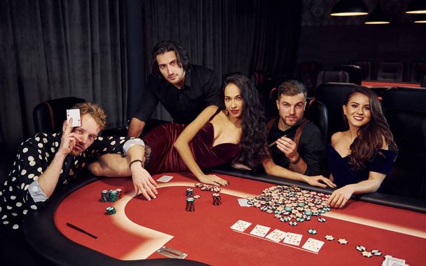 Woman lying down on table. Group of elegant young people that playing poker in casino together. - Fotó, kép