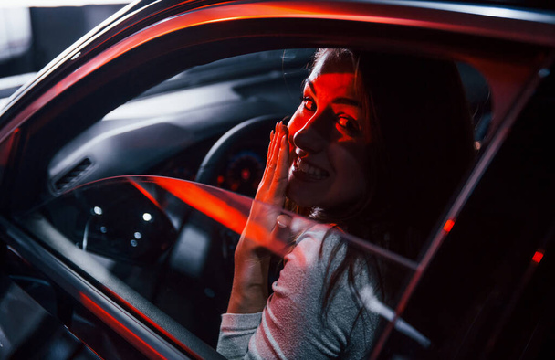 Young woman is inside of brand new modern automobile with red lighting. - Foto, Imagen