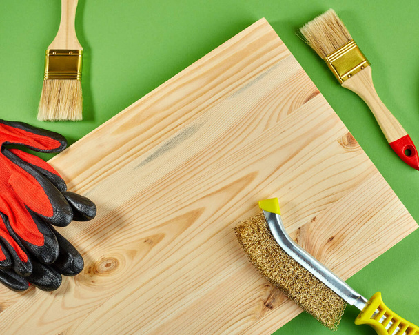 Εργαλεία ξυλουργικής σε πράσινο φόντο. Ξύλινη σανίδα, βούρτσα ξύλου, βούρτσες και γάντια εργασίας. Θέα από ψηλά. Επίπεδη - Φωτογραφία, εικόνα