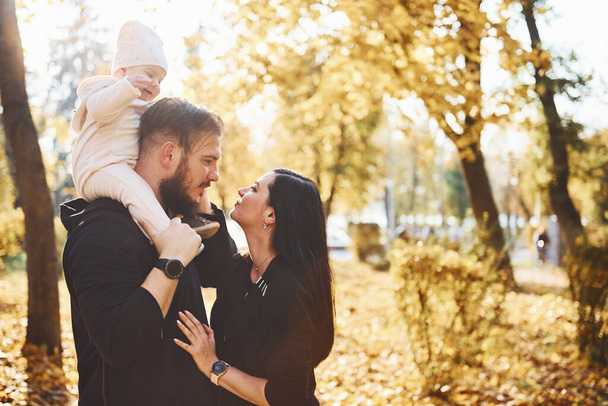 Cheerful family having fun together with their child in beautiful autumn park. - Foto, imagen