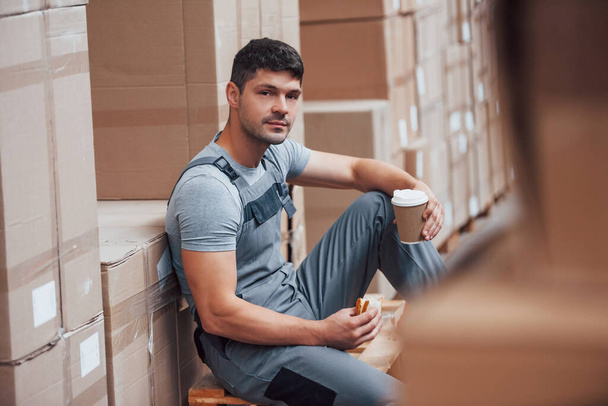 Storage worker sits and have a break. Eats sandwitch and drinks coffee. - 写真・画像