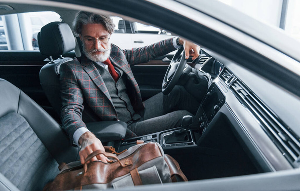 Fashionable senior man with grey hair and mustache on vacation with bag inside modern automobile. - Valokuva, kuva