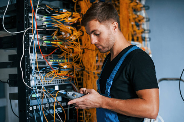 Young man in uniform have a job with internet equipment and wires in server room. - Valokuva, kuva