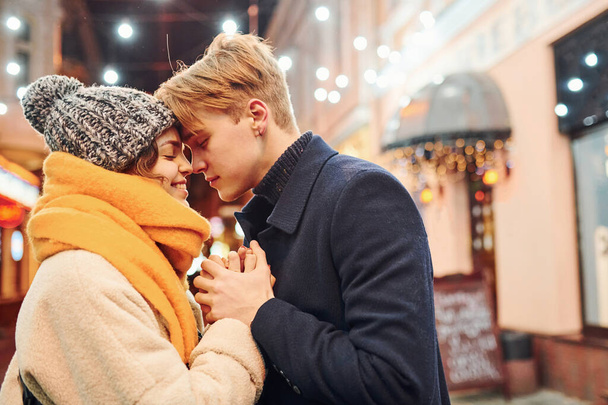 Closeness of the people. Happy young couple in warm clothes is on christmas decorated street together. - Foto, Imagen