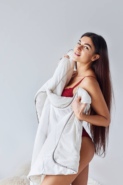 Woman in red underwear covering her body by towel in the studio against white background. - Fotó, kép