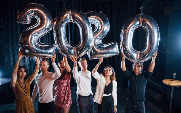Cheerful group of people with drinks and balloons in hands celebrating new 2020 year. - 写真・画像