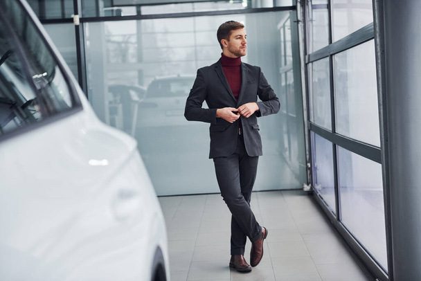 Young business man in luxury suit and formal clothes is indoors near the car. - Photo, Image