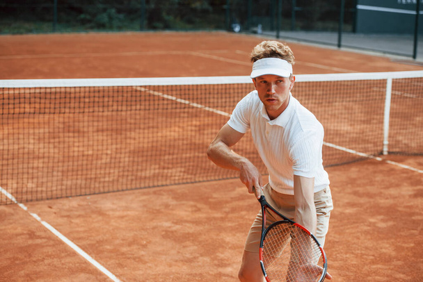 Young tennis player in sportive clothes is on the court outdoors. - Φωτογραφία, εικόνα
