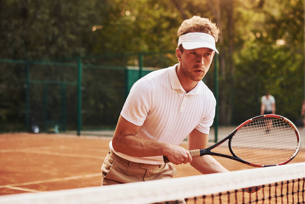 Holds racket in hands. Young tennis player in sportive clothes is on the court outdoors. - Foto, immagini