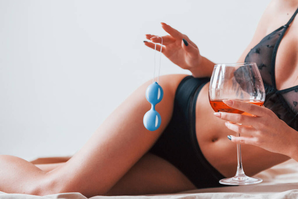 Young woman with wine and blue sex balls in hands. Conception of intimacy. - 写真・画像