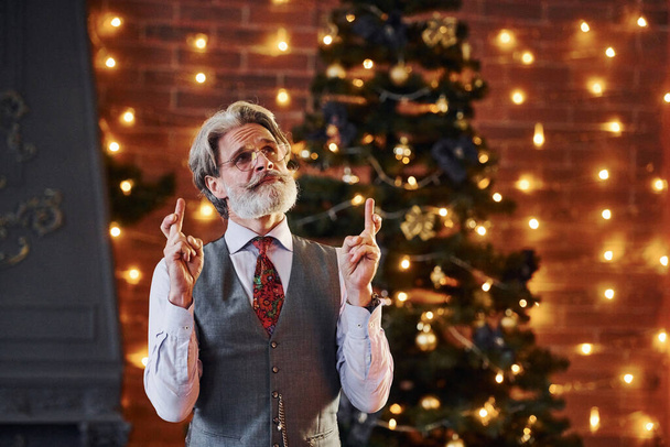 Portrait of stylish senior with grey hair and beard in jacket and white shirt is in decorated christmas room. - Fotó, kép