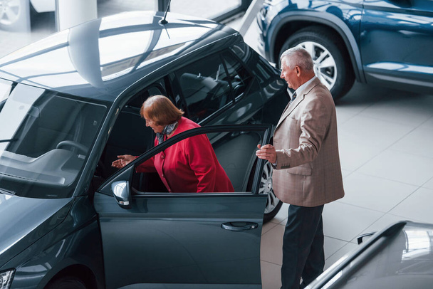 Aged man in formal wear supporting woman in choosing automobile. - Fotoğraf, Görsel