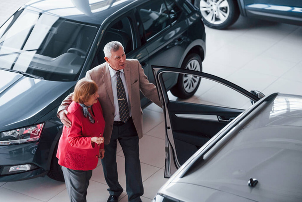 Aged man in formal wear supporting woman in choosing automobile. - Фото, зображення