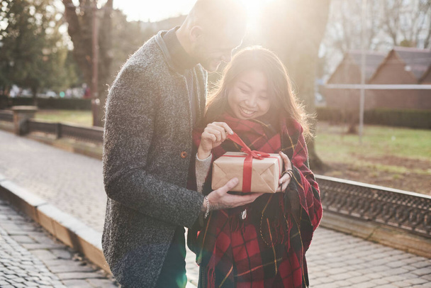 Beautiful sunlight. Happy multiracial couple together outdoors in the city with gift box in hands. - Fotografie, Obrázek