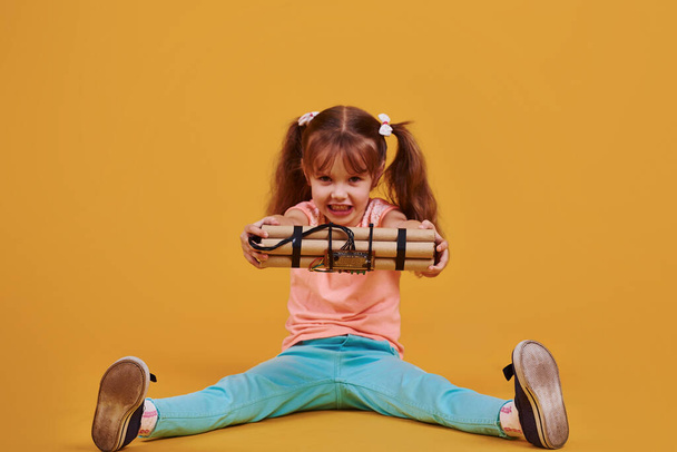 Little girl with explosive in the studio against yellow background. - Foto, Imagen
