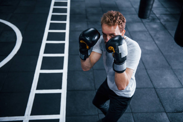 Young man in white shirt and boxing protective gloves doing exercises in gym. - Fotografie, Obrázek