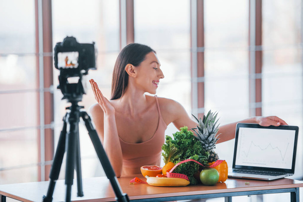 Young fitness vlogger doing video indoors by sitting near table with healthy food. - 写真・画像