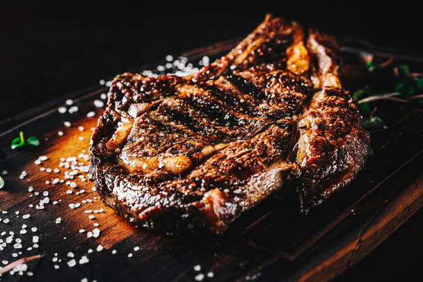 Grilled Ribeye Steak on bones on wooden board, prime cowboy steak on dark background - Photo, image