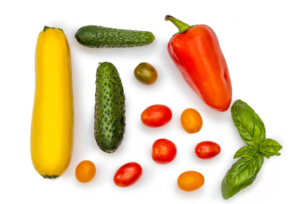 Plantaardig plat: komkommers, courgettes, kerstomaten, een takje basilicum en paprika 's op een wit bord. - Foto, afbeelding