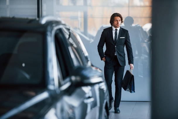 Portrait of handsome young businessman in black suit and tie and with shopping bag near the modern car. - Foto, immagini