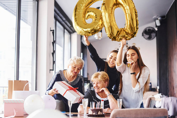 Balloons with number 60. Senior woman with family and friends celebrating a birthday indoors. - Foto, Imagem