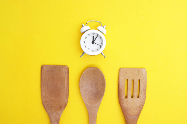 Un conjunto de platos de bambú y un reloj vintage blanco sobre un fondo amarillo brillante. Concepto de cocina. - Foto, Imagen