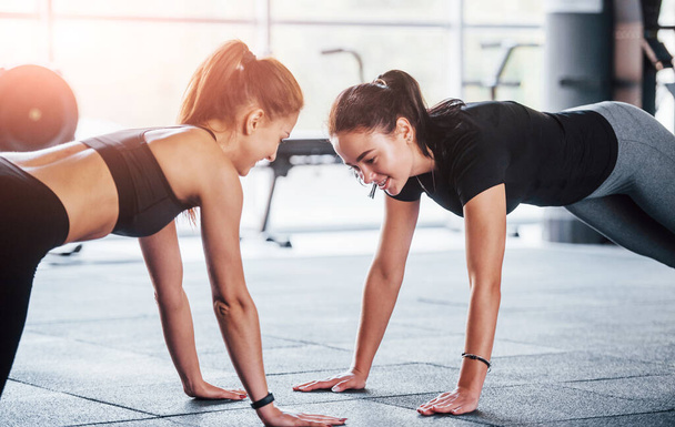 Two young girls in sportive clothes is in the gym doing exercises together. - Foto, Imagen