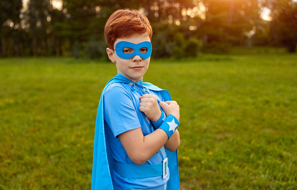 Cute boy in superhero outfit looking at camera in green park - Фото, зображення