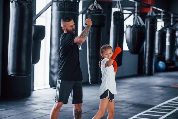 Basic punches. Young tattooed boxing coach teaches cute little girl in the gym. - Fotografie, Obrázek
