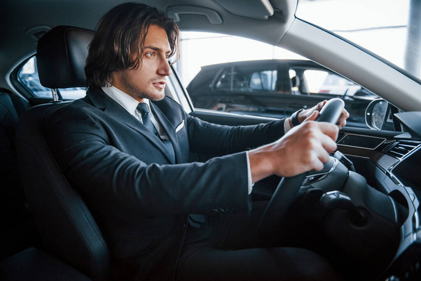 Young businessman in black suit and tie driving modern automobile. - Fotoğraf, Görsel