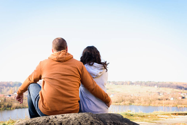 joven pareja abrazando y sentado cerca, espalda, en una gran roca en el fondo del lago  - Foto, imagen